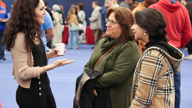 A proffessor speaking with a parent and a student at a open house event